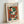 Framed vintage-style art poster featuring Henri Matisse's abstract modernist painting with geometric shapes in vibrant colors including green, orange, red, blue, and cream. The artwork shows angular, overlapping forms suggesting a stylized figure or portrait. Displayed in a light wooden frame leaning against a white wall, creating soft shadows. The poster has French text at the top and showcases Matisse's characteristic bold color palette and simplified forms.