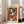 May include: Framed Henri Matisse art print leaning against white wall beside beige sectional sofa in bright living room. Abstract figure wearing colorful hat rendered in bold geometric shapes - vibrant oranges, greens, blues, and cream tones. Light wood frame, hardwood floors, large windows with natural sunlight streaming in.