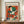 May include: Framed Henri Matisse exhibition poster featuring an abstract figure in colorful geometric shapes - orange, green, red, white, and black patches forming a stylized person wearing a hat. The poster has cream background with black text at top. Displayed on a wooden sideboard next to white ceramic vase and stacked books against cream wall with white molding.