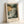 May include: Framed poster print leaning against white wall showing dramatic coastal seascape with stormy skies in golden yellow and dark green tones, rocky cliffs on right side, turbulent ocean waves, and flying birds. Text reads "HENRI MATISSE PARIS" below artwork. Natural wood frame with light finish sits on white surface with soft shadows.
