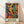 May include: Framed poster print featuring vibrant abstract figures in flowing motion with silhouetted heads and colorful bodies in blues, greens, oranges, and purples. The artwork shows dancing forms against a bright background, displayed in a light wooden frame leaning against a white wall on wooden flooring with natural window light creating shadows.