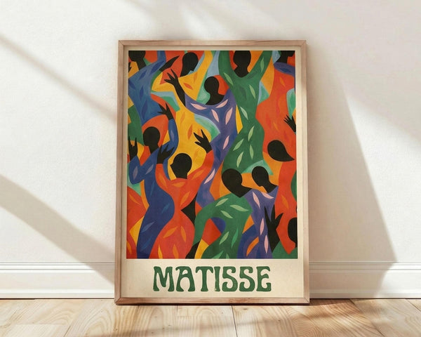 May include: Framed poster print featuring vibrant abstract figures in flowing motion with silhouetted heads and colorful bodies in blues, greens, oranges, and purples. The artwork shows dancing forms against a bright background, displayed in a light wooden frame leaning against a white wall on wooden flooring with natural window light creating shadows.