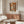 May include: Henri Matisse forest poster print with autumn orange and brown tones displayed above a wood credenza in minimalist living room. White curved chair, glass coffee table, and modern lamp complete the neutral decor scene with warm natural lighting.