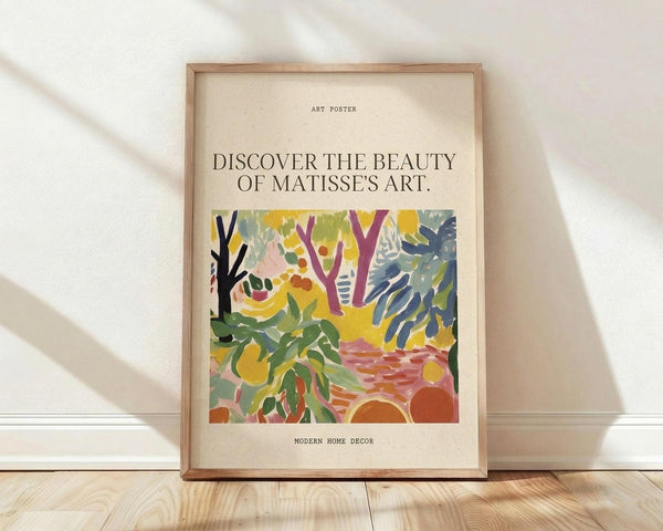 May include: Framed art poster featuring a vibrant Matisse-style landscape with colorful trees, foliage and abstract forms in yellows, greens, purples and oranges. The cream-colored poster has "ART POSTER" at top, "DISCOVER THE BEAUTY OF MATISSE'S ART" as main text, and "MODERN HOME DECOR" at bottom. Natural wood frame sits against white textured wall on light wooden flooring with soft shadows.