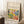 May include: Framed art poster leaning against white wall on textured white rug. Features colorful abstract landscape with green foliage, purple tree branches, yellow and blue brushstrokes, and orange circular elements in Matisse's distinctive style. Text reads "Discover the Beauty of Matisse's Art" above artwork and "Modern Home Decor" below. Natural wood frame, cozy room setting with coffee cup on wooden block and beige blanket visible.