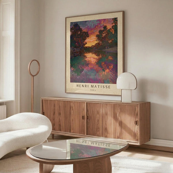 May include: colorful landscape poster with vibrant sunset sky and water reflection, displayed above wooden credenza in modern living room with cream walls, white sculptural chair, glass coffee table, and warm natural lighting creating soft shadows
