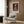 May include: Henri Matisse poster print in light wood frame hanging on wood-paneled wall above beige upholstered armchair. The artwork shows a colorful landscape with trees reflected in water, featuring vibrant purples, oranges, and greens in an impressionistic style. Modern reading corner with geometric patterned pillow, brass floor lamp, and round side table with open book.