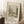 May include: Framed vintage botanical print leaning against white wall on textured cream rug. The sepia-toned artwork shows a peaceful riverside scene with trees, small buildings, and water. Light wooden frame, displayed next to wooden side table with white coffee cup and saucer. Soft natural lighting creates shadows across the minimalist room setting.