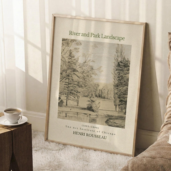 May include: Framed vintage botanical print leaning against white wall on textured cream rug. The sepia-toned artwork shows a peaceful riverside scene with trees, small buildings, and water. Light wooden frame, displayed next to wooden side table with white coffee cup and saucer. Soft natural lighting creates shadows across the minimalist room setting.