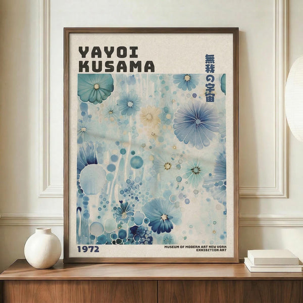 May include: Framed exhibition poster featuring blue watercolor floral patterns and polka dots with "YAYOI KUSAMA" text and "1972" date, displayed on wooden credenza next to white ceramic vase and stacked books in room with cream walls and white trim molding.