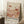 May include: Framed art print leaning against white wall in cozy room setting with coffee cup on wooden block and knit blanket. The poster features abstract botanical illustration in warm coral, peach and cream tones with polka dot mushrooms, fan-shaped plants, and organic forms. Text reads "YAYOI KUSAMA" and Japanese characters with "KYOTO" below in modern typography on cream background.
