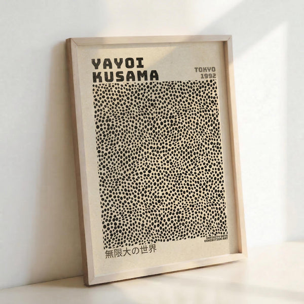 May include: Framed poster with cream background featuring bold black text "YAYOI KUSAMA" at top, "TOKYO 1992" in upper right corner, and dense pattern of small black dots covering most of the design. Japanese text appears at bottom left. Light wooden frame sits against white wall, casting subtle shadow.