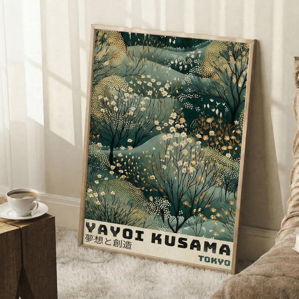 May include: Framed poster with abstract botanical artwork featuring flowing green and teal organic shapes, delicate white flowers, and dotted patterns in Kusama's signature style. Text reads "YAYOI KUSAMA" with Japanese characters and "TOKYO" below. Light wood frame leans against white wall next to wooden stool with coffee cup, cream textured rug visible.