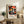 May include: Framed poster featuring colorful mushrooms with red and orange spotted caps against a black dotted background, displayed on a rustic wooden console table beside a fern plant, ceramic vase, and leather chair in a neutral-toned living room setting.