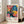 May include: Framed colorful poster featuring vibrant tropical flowers and dotted patterns in pink, blue, yellow, and orange hues, displayed against a white wall in a bright living room with beige sofa, white rug, and large windows with natural lighting