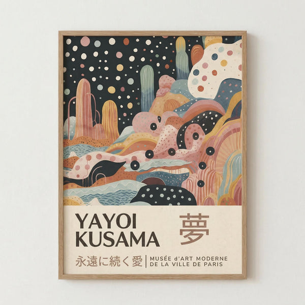 Framed art print featuring Yayoi Kusama's distinctive polka dot style with abstract landscape elements. The artwork shows colorful organic shapes in soft pastels - pink, yellow, green, and coral - against a black starry sky dotted with white circles. Bottom section contains flowing, layered forms resembling hills or waves with scattered dots throughout. Japanese text and museum attribution appear on cream-colored border below the main image. Natural wood frame displayed against white wall.