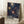 May include: Framed poster with navy blue background featuring colorful radiating dot patterns in cream, orange, and blue tones, displayed in light wood frame leaning against white wall next to coffee cup on wooden stool and cozy textured blanket in bright room with natural lighting