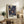 May include: Framed art print with dark blue background featuring colorful radiating sunburst patterns in yellow, orange, and white dots. Print displays "YAYOI KUSAMA" and museum text at bottom. Wooden frame sits on rustic wood sideboard next to fern plant, ceramic vase, and books in neutral-toned living room setting.
