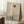 May include: Minimalist poster art in light wooden frame leaning against white wall, featuring bare black tree silhouette with rust-colored sun on beige textured background. Soft natural lighting creates window shadows across the scene. White coffee cup on wooden block and cream blanket visible nearby on white fuzzy rug.