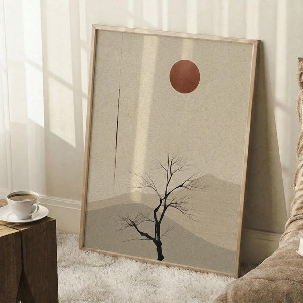 May include: Minimalist poster art in light wooden frame leaning against white wall, featuring bare black tree silhouette with rust-colored sun on beige textured background. Soft natural lighting creates window shadows across the scene. White coffee cup on wooden block and cream blanket visible nearby on white fuzzy rug.