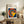 May include: Framed Bauhaus poster with colorful concentric circles in red, yellow, blue, and white on navy background, displayed on rustic wooden sideboard alongside books, ceramic vase, and fern plant in modern living room setting with beige armchair and neutral walls