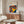 May include: Bauhaus poster with colorful concentric circles in red, yellow, blue, and orange on navy background, displayed above wooden sideboard in minimalist room with white curved chair, glass coffee table, and modern lighting