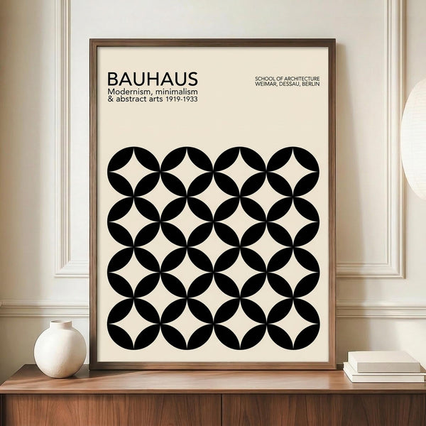 May include: Framed modernist poster with black geometric circle pattern on cream background, displayed on wooden sideboard with small white ceramic vase and books, against white wainscoted wall. The minimalist design features repeating overlapping circles creating diamond shapes between them.