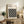 May include: Framed Bauhaus poster with geometric black circles pattern on cream background, displayed on rustic wooden sideboard alongside fern plant, ceramic vase, and brown leather chair in neutral-toned living room setting.