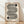 May include: Framed geometric poster with black striped wavy lines forming an S-shaped pattern on cream background, featuring two black circles with concentric line details, displayed against white textured wall on light wood floor with natural window light shadows