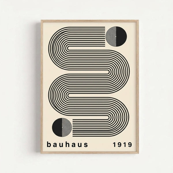 May include: Framed geometric art print featuring flowing black and white curved lines forming an abstract S-shaped pattern with two circular elements, displayed against a white wall. The minimalist design uses parallel stripes and concentric circles, with "bauhaus 1919" text at bottom. Light wood frame surrounds cream-colored background.