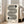 May include: Large framed print with black and white geometric design featuring flowing curved lines and circular elements on cream background, displayed on wooden floor against white wall next to beige upholstered sofa in bright living room with natural light from windows