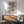 May include: Framed Bauhaus-inspired poster with black geometric wavy lines and circles on cream background, displayed above wooden sideboard in modern living room with mint green upholstered chair, white table lamp, and natural lighting casting shadows on white walls.