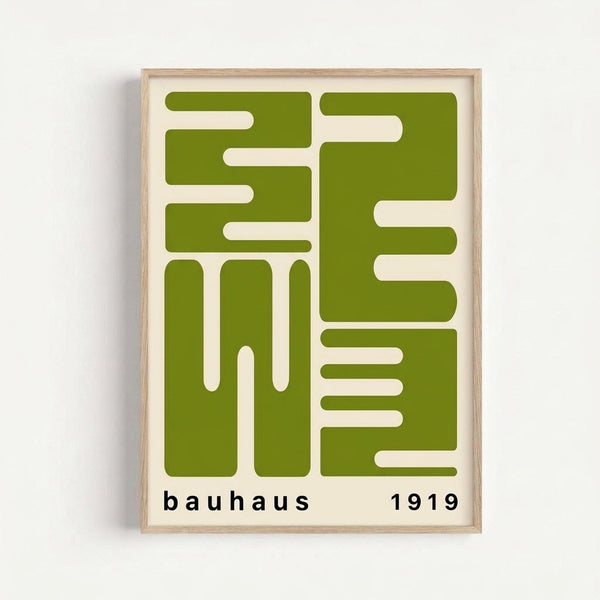 Geometric abstract poster with bold olive green shapes on cream background, featuring interlocking rectangular and linear forms. The design includes "bauhaus" and "1919" in black text at bottom. Displayed in natural wood frame against white wall.