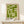 May include: Framed geometric poster with olive green abstract shapes forming interlocking patterns on cream background, displayed on light wood console table against white wall. Small wrapped gift box with evergreen sprig sits nearby. Design features bold angular forms and negative space in mid-century modern style.