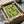 May include: Green and cream geometric Bauhaus poster in black frame being unpacked from cardboard box with tissue paper, showing bold angular shapes and "1919" text, displayed on white surface with wooden rolling pin nearby