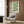 May include: Framed geometric poster with green wavy lines and black circular elements on cream background, displayed above beige upholstered chair with patterned pillow in modern living room setting with wood paneled walls, gold floor lamp, and dark round side table with open book.