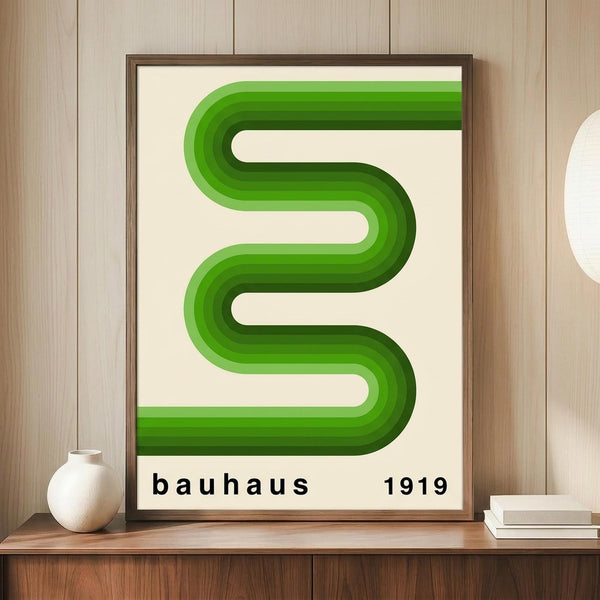 May include: Framed geometric poster with flowing green gradient ribbons forming curved S-shaped lines on cream background, displayed on wooden shelf next to small white ceramic vase and stacked books against light wood paneled wall