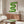 May include: Green wavy geometric design poster with "bauhaus 1919" text, displayed in thin wooden frame above mid-century walnut credenza. Modern white sculptural chair and glass coffee table with wooden base visible in bright, minimalist room setting with white walls and natural lighting.