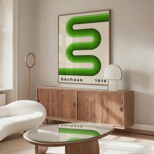 May include: Green wavy geometric design poster with "bauhaus 1919" text, displayed in thin wooden frame above mid-century walnut credenza. Modern white sculptural chair and glass coffee table with wooden base visible in bright, minimalist room setting with white walls and natural lighting.