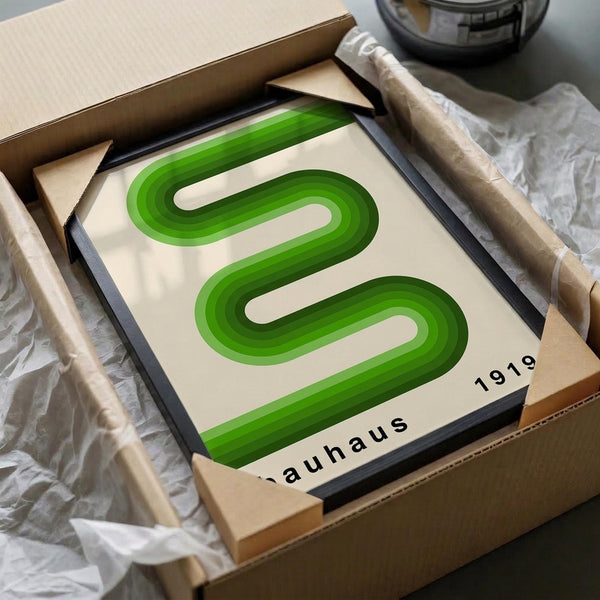 May include: Green geometric poster with curved serpentine design in gradient shades from light to dark green on cream background, displayed in black frame inside cardboard shipping box with protective padding, surrounded by white tissue paper and wooden dowels for packaging