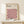 May include: Framed Bauhaus poster with geometric cube pattern in pink, orange, black and cream colors, displayed on light wood surface next to small white wrapped gift with greenery. Modern minimalist room setting with neutral walls and natural lighting.