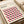 May include: Framed Bauhaus-style poster with geometric cube pattern in pink, orange, black and cream colors, displayed on light wooden surface next to rolled paper tubes. The minimalist design features repeating 3D cube illusion creating depth and movement across the composition.