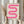 May include: Hands holding a framed poster featuring a pink gradient serpentine ribbon design against cream background, with "bauhaus 1919" text below. Light wood frame, dried pampas grass visible to left, soft beige curtains and neutral interior setting. Person wearing cream colored ruffled sleeve top.