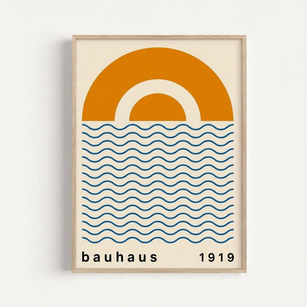 A framed minimalist poster featuring a large orange semi-circle resembling a sun with a smaller concentric arc inside, positioned above horizontal blue wavy lines representing water. The design uses a cream background with "bauhaus" and "1919" text at the bottom. The artwork is displayed in a light wood frame against a white wall.
