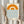 May include: Person in beige ruffled sleeves holding framed minimalist poster featuring orange semicircular sun design above blue wavy lines representing water, with "bauhaus 1919" text below. Light wooden frame against neutral curtained background with dried pampas grass visible on left side.