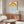 May include: Framed poster with orange semicircle sun design and blue wavy lines representing water, displayed above a wooden sideboard in a minimalist room setting with white curved chair, glass coffee table, and neutral walls