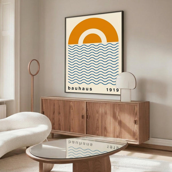May include: Framed poster with orange semicircle sun design and blue wavy lines representing water, displayed above a wooden sideboard in a minimalist room setting with white curved chair, glass coffee table, and neutral walls