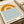 May include: Framed minimalist poster with orange semicircular sun and blue wavy lines representing water, displayed on cream colored surface next to rolled papers. The design features "bauhaus" and "1919" text in black lowercase letters on an off-white background within a thin wooden frame.