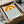 May include: Framed minimalist art print in black frame, packed in cardboard box with tissue paper. Design features orange semicircular sun and blue wavy lines representing water on cream background, with "1919" and "bauhaus" text at bottom. Wooden dowels and packaging materials visible around shipping box.