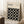May include: Framed Bauhaus poster with black background and white circles arranged in geometric grid pattern, leaning against white wall corner. Light wood frame, cream matting, minimalist typography at top. Wooden block with white coffee cup nearby on textured rug in bright, airy room setting.